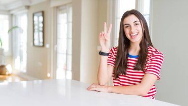 Güzel genç kadın rahat çizgili t-shirt mutlu yüz zafer işareti yapıyor kamera göz kırpıyor ile gülümseyen giyiyor. İki numara.