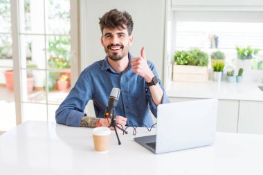 Genç adam kayıt podcast kullanarak mikrofon ve dizüstü bilgisayar el ile jest kadar mutlu thumbs yapıyor. Başarı göstererek kameraya bakarak ifadeyi onaylama.