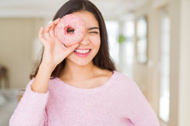 Göz üzerinde pembe çörek bakarak gülümseyen güzel genç kadın