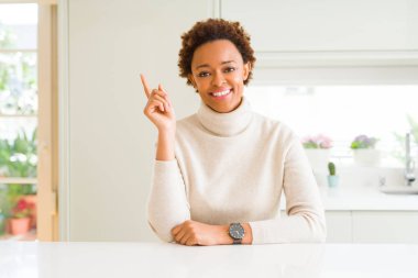 Kameraya bakarak yan el ve parmak ile işaret eden genç güzel Afrikalı-Amerikalı kadın evde yüzünde kocaman bir gülümseme ile.