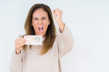 İzole arka plan üzerinde 10 pound banka notu tutan orta yaş kadın rahatsız ve öfke, çılgın ve yükseltilmiş el, öfke kavramı ile bağırarak bağırma sinirli