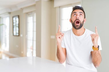 Casual beyaz t-shirt evde hayret ve yukarıya bakıp parmakları ile işaret şaşırttı ve silah kaldırdı İspanyol yakışıklı.