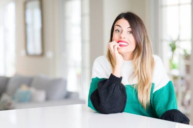 Evde kış kazak giyen genç güzel kadın stresli ve gergin elle çivi ısırma ağzına bakıyor. Anksiyete sorunu.