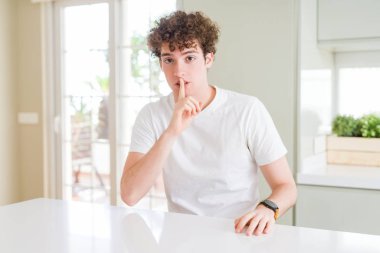 Evde beyaz t-shirt giyen genç yakışıklı adam dudaklarında parmak ile sessiz olmanı. Sessizlik ve gizli kavramı.