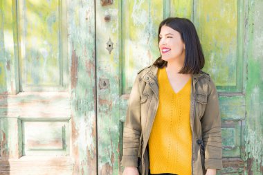 Güneşli bir günde şehir sokakta yürürken duvardaki, kendinden emin ve neşeli yaslanmış gülümseyen güzel genç kadın