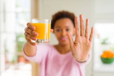 Genç Afro-Amerikan kadın driking portakal suyu evde dur işareti ciddi ve kendine güvenen ifade ile yapıyor açık el ile savunma hareketi