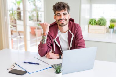 Bilgisayar laptop ve işaret ve başparmak kadar mutlu yüz gülümseyen tarafı ile gösterilen defter kullanan genç öğrenci adam