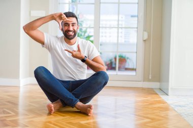 Evde oturan rahat t-shirt giyen yakışıklı İspanyol adam mutlu yüz ile eller ve parmaklar ile çerçeve yapma gülümseyen. Yaratıcılık ve Fotoğrafçılık konsepti.