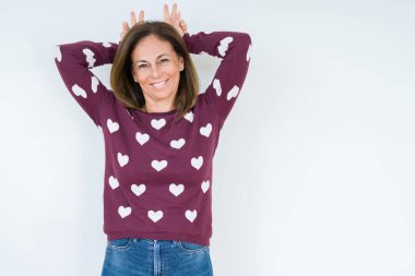 Güzel orta yaş kadın izole arka plan üzerinde kalp kazak giyiyor Bunny kulakları olarak kafa parmakları ile komik ve deli poz, neşeli gülümseyen