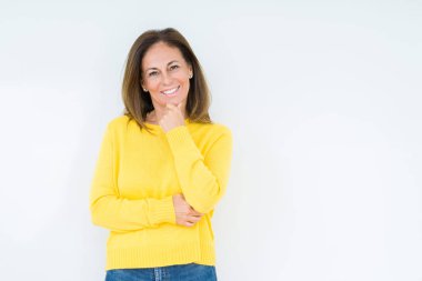 Emin çapraz kollar ve çeneme kaldırdı el ile gülümseme ile kameraya bakarak izole arka plan üzerinde sarı kazak giyen güzel orta yaş kadın. Pozitif düşünce.