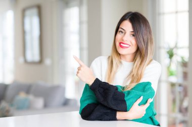 Evde kış kazak giyen genç güzel kadın el parmak ile gösterilen reklam, ciddi ve sakin yüz tarafına işaret.