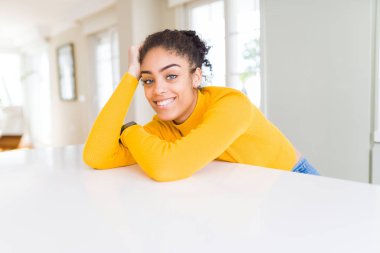 Güzel genç Afrikalı Amerikalı kadın neşeli masada rahat eğilerek gülümseyen