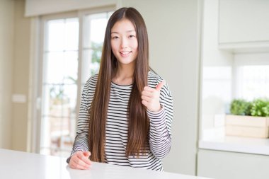 Güzel Asyalı kadın çizgili kazak giyen mutlu thumbs el ile jest yapıyor. Başarı göstererek kameraya bakarak ifadeyi onaylama.