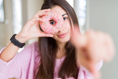 Pembe çikolata cips yeme güzel genç kadın kamera ve sizin için parmak ile işaret çörek, ön el işareti, pozitif ve emin jest