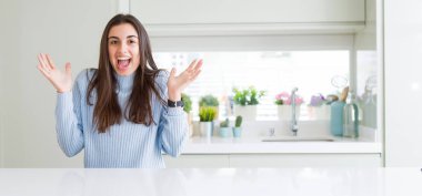 Güzel genç kadın evde beyaz masaya oturan geniş açı resim çılgın ve başarı için hayran kaldırdı Kollarını açarak kutluyor ve heyecanlı çığlık gözleri açık. Kazanan kavramı