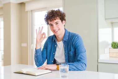 Genç adam evde kitap okurken parmak, mükemmel sembolü ile ok işareti yapıyor