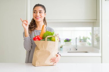 Küçük bir kadın tutan kağıt çanta dolu bakkaliye çok mutlu işaret ile el ve parmak yan