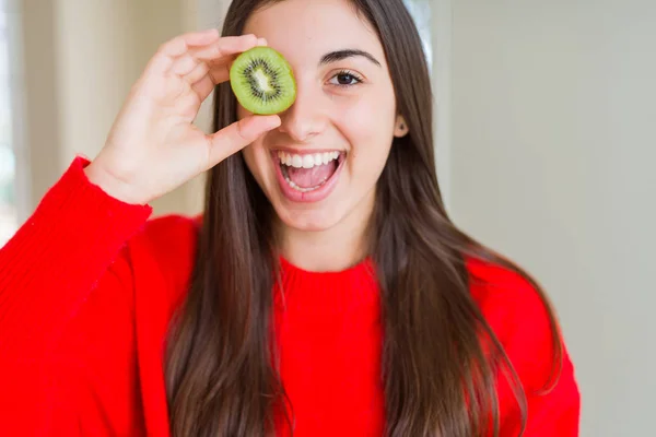 美しい若い女性が立って幸せな顔で半分新鮮な緑のキウイを食べて 歯を示す自信を持った笑顔で微笑んで — ストック写真
