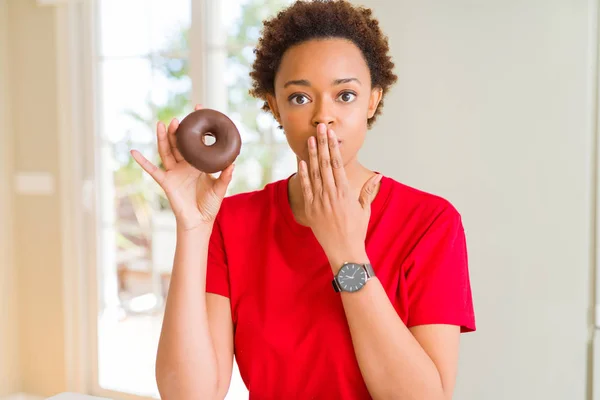 年轻的非洲裔美国妇女吃巧克力甜甜圈覆盖嘴与手震惊的耻辱 表达恐惧 害怕在沉默中 秘密的概念 — 图库照片