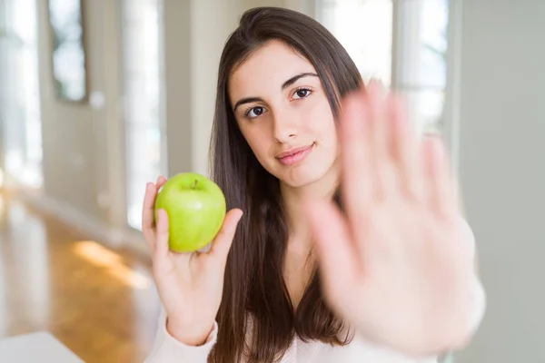 美丽的年轻女子吃健康的绿色苹果水果与张开的手做停止标志与认真和自信的表达 防御姿态 — 图库照片
