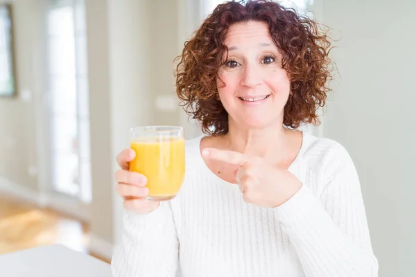 高级女子滴下一杯新鲜的橙汁非常高兴地指着手和手指 — 图库照片