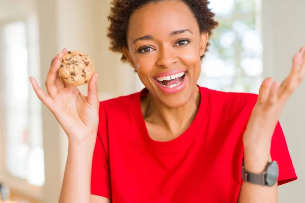 Young african american woman eating chocolate chips cookies very happy and excited, winner expression celebrating victory screaming with big smile and raised hands