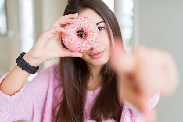 美しい若い女性は カメラに指で指しているピンクのチョコレートチップスドーナツを食べて あなたに 手のサイン 正面からの正と自信を持ってジェスチャー — ストック写真