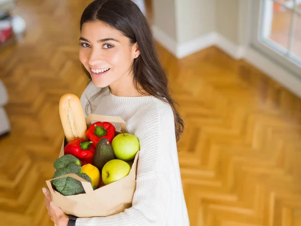 新鮮な食料品を自宅でいっぱいに紙袋を抱えた美しい若い女性 — ストック写真