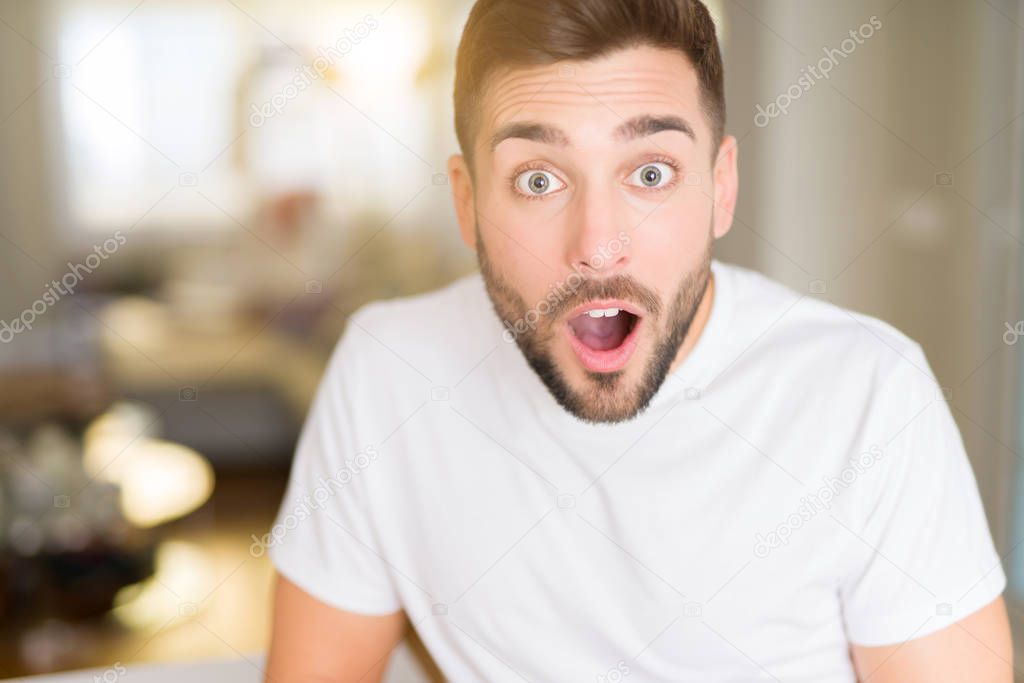 Young handsome man wearing casual white t-shirt at home afraid and shocked with surprise expression, fear and excited face.