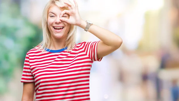 Young beautiful blonde woman over isolated background doing ok gesture with hand smiling, eye looking through fingers with happy face.