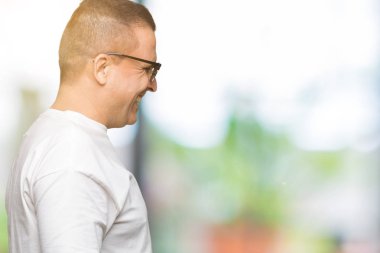 Orta yaş Arap adam wearig beyaz t-shirt ve izole arka plan üzerinde güneş gözlüğü yan arıyor, güvenli bir gülümseme ile doğal yüz ile profil poz rahatlayın.