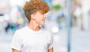Uzak tarafına yüzünde, doğal ifade gülümseme ile seyir casual beyaz t-shirt giyen afro saçlı Genç yakışıklı adam. Kendine güvenen gülüyor.
