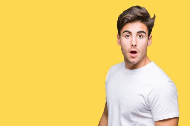 Korkuyor ve şok sürpriz ifade, korku ve heyecan yüz ile izole arka plan üzerinde beyaz t-shirt giyen genç yakışıklı adam.