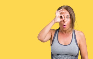 Sürpriz yüz, göz parmaklarının arasından seyir spor kıyafetlerle ok jest yapıyor izole arka plan üzerinde güzel orta yaş kadın şok. İmansız ifade.
