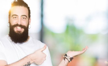 Uzun saç ve sakal casual beyaz t-shirt gösteren giyen genç hipster adamla palm el ve yukarıya, mutlu ve neşeli gülümseyen baş parmakları Tamam jest yapıyor