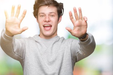 İzole arka plan üzerinde sweatshirt giyen genç yakışıklı sportif adam gösteren ve parmak numarası dokuz ile işaret kadar güven ve mutlu gülümseyen.