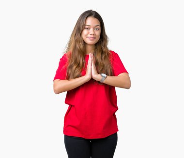 Birlikte emin gülümseyen bağışlanmak ellerle dua izole arka plan üzerinde kırmızı t-shirt giyen genç güzel esmer kadın.