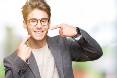 Kendinden emin gösterilen ve işaret parmakları diş ve ağız ile gülümseyen izole arka plan üzerinde gözlük takan genç iş adamı. Sağlık kavramı.