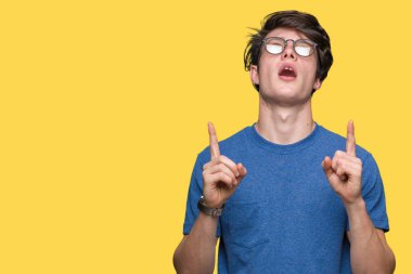 Yakışıklı delikanlı hayrete ve yukarıya bakıyor ve parmakları ile işaret ve silah kaldırdı sürpriz izole arka plan üzerinde gözlük.