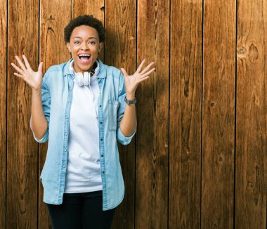 Üzerinde kulaklık giyen genç Afro-Amerikan kadın deli kutluyor arka plan izole ve silah ile başarı için yükseltilmiş ve açık gözleri heyecanlı çığlık hayrete düşürdü. Kazanan kavramı