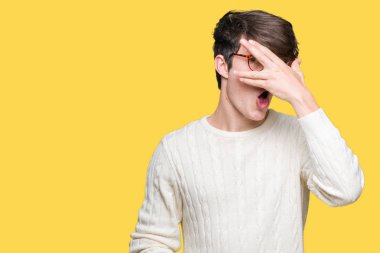 Mahcup ifadeyle parmaklarımın arasından seyir yüz ve gözler el ile kapsayan şok bakmak izole arka plan üzerinde gözlük takan genç yakışıklı adam.