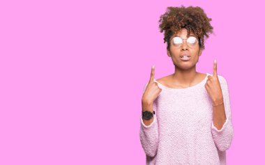 Güzel genç Afro-Amerikan kadın hayrete ve yukarıya bakıyor ve parmakları ile işaret ve silah kaldırdı sürpriz izole arka plan üzerinde gözlük.