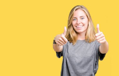 El ile pozitif jest yapıyor onaylama izole arka plan üzerinde büyük boy rahat t-shirt giyen güzel ve genç birbayan başparmak gülümseyen ve başarı için mutlu. Kamera, kazanan jest arıyorsunuz.