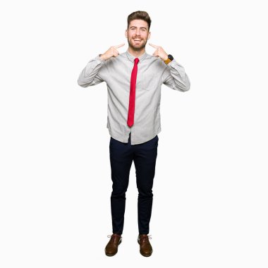 Kendinden emin gösterilen ve işaret parmakları diş ve ağız ile gülümseyen genç yakışıklı iş adamı. Sağlık kavramı.