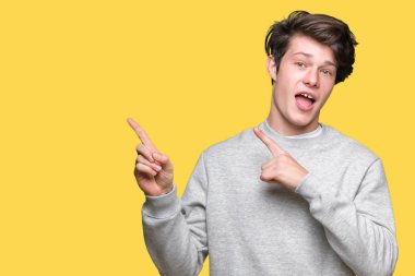 Gülümseyen ve iki elleri ve parmakları ile tarafına işaret kamera bakarak izole arka plan üzerinde sweatshirt giyen genç yakışıklı sportif adam.