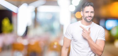 İzole arka neşeli bir gülümseme ile yüz el ve parmak kadar mutlu ve doğal ifade yüzünde yanında işaret içinde Casual beyaz t-shirt giyen genç adam