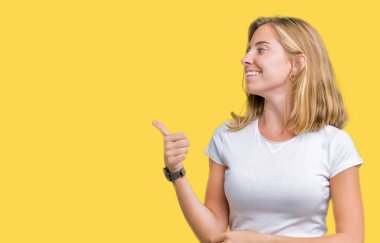 Rahat giyen güzel genç kadın tarafa jest yapıyor gülümseyen beyaz t-shirt gurur, seyir izole arka plan üzerine yaşasın