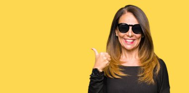 Seyir ve başparmak yanında yukarıyı mutlu yüz ile gülümseyen güneş gözlüğü takıyor güzel orta yaş kadın.