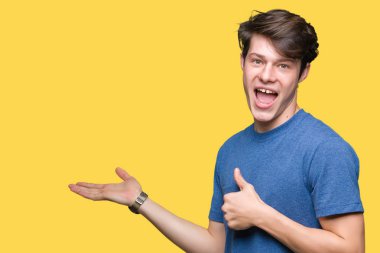 İzole arka plan gösteren palm el üzerinde mavi t-shirt giyen ve yukarıya, mutlu ve neşeli gülümseyen baş parmakları Tamam jest yapıyor yakışıklı delikanlı