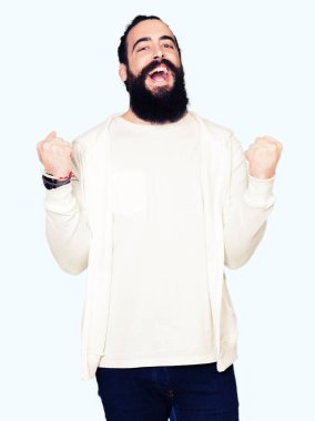Uzun saç ve sakal kutluyor sportif sweatshirt giyen genç adamla şaşırttı ve başarı için kaldırdı kollarını açarak hayret ve gözleri açık. Kazanan kavramı.